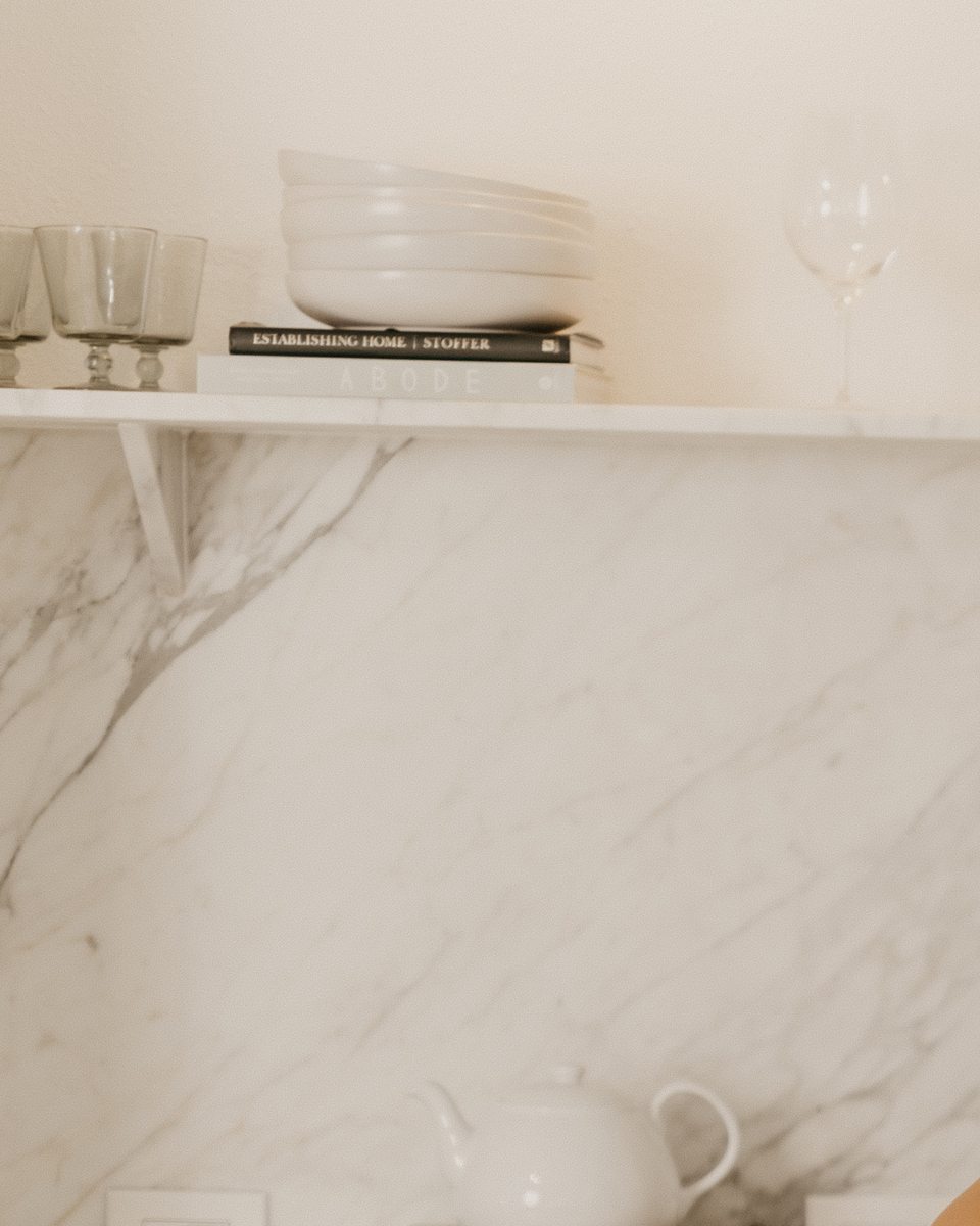 A small stack of design books styled on an ivory kitchen shelf.