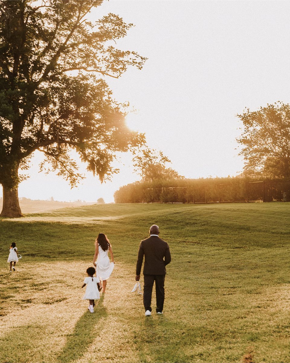 The NikaDiwa family walking together through a sunlit field, photographed from behind.